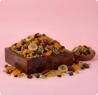 Wooden bowl filled with a mix of dried fruits and nuts on a pink background